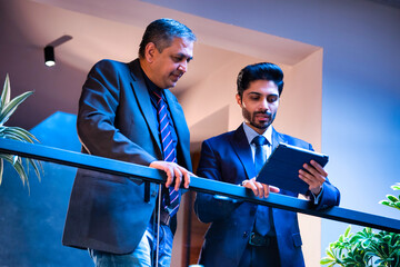 Two Indian executives sharing ideas using tablet near glass partition in modern corporate office