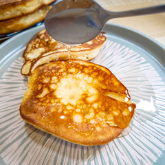 pancakes and honey Pour syrup over pancakes from silver syrup pitcher. Homemade pancakes in a gray plate are poured with a thin stream of slow motion honey. Medium plan.