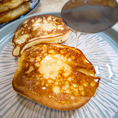 pancakes and honey Pour syrup over pancakes from silver syrup pitcher. Homemade pancakes in a gray plate are poured with a thin stream of slow motion honey. Medium plan.