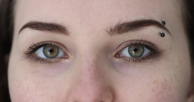 Attractive woman eyes with black eyebrow piercing winks playfully. Bright green eyes gleam as female throws mischievous wink. Slow motion
