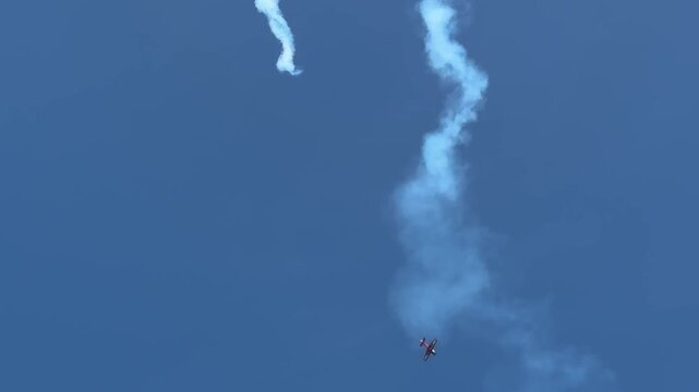 A skilled pilot performs a thrilling acrobatic loop and dive maneuver in a stunt plane, leaving a long white smoke trail across the clear blue sky during an airshow