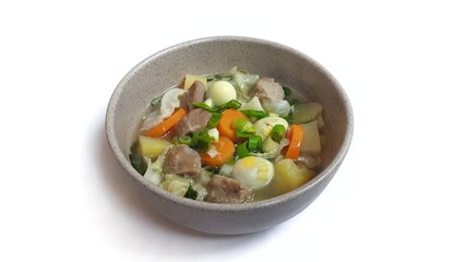 Sayur sop or vegetable soup, is an Indonesian food served on brown bowl. Isolated on white background. Food presentation photography