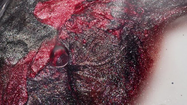 Macro view of red and black glitter ink slowly spreading across a white surface, forming graphic contrasts.