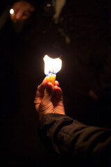 A person is holding a lit candle in their hand while it is dark
