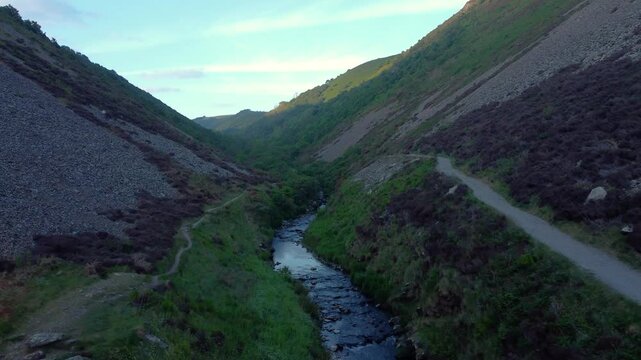 Fast Moving Aerial Heading Up River with Hiking Paths on Each Side at Sunrise with Sunlight on Top of Valley. Natural Bird's Eye View. Drone Footage.