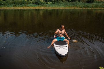 Man rides on a SUP board on the river in the middle of the forest, summer active outdoor recreation 