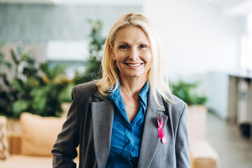Smiling businesswoman wearing pink ribbon supporting breast cancer awareness