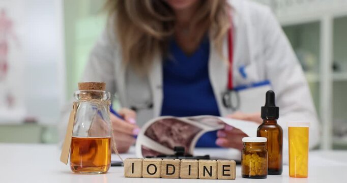 Medical professional reviews ultrasound scans near Iodine on wooden blocks. Bottles with liquids suggest focus on chemical element and applications