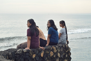 Four teenage girls sit calmly on the sandy beach, admiring the gentle waves and coastal scenery under the warm morning sunlight.