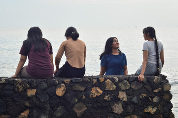A teen girl leaves the raised beach edge to join her friend by the sea for a morning chat on the breezy shore.
