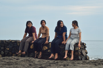 A group of four teen girls enjoying a relaxed morning, sitting together on the beach, chatting while enjoying the waves and fresh sea breeze.