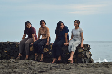 A peaceful morning scene of four teenage girls gathered at the beach, bonding and smiling together while seated on the soft sand near the shoreline.