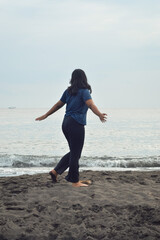 A teen girl strolls freely on the soft morning sand, arms wide open and hair flowing, enjoying the breeze and sound of waves at the beach.