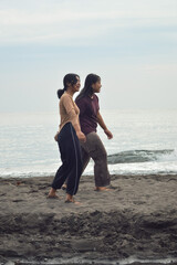 Two teen girls walk hand in hand along the sunny beach, laughing together while enjoying the peaceful morning and gentle waves.
