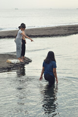 On the beach, one curious girl points to something in the shallow water while her friends look on, all sharing a moment of fascination and play.