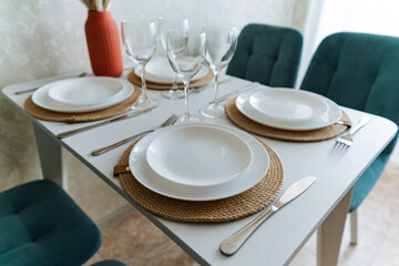 An incredibly elegant dining room table is meticulously and beautifully set with a stunning array of plates, fine glasses, and shiny silverware wonderfully artfully arranged on its surface