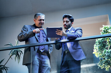 Two Indian executives sharing ideas using tablet near glass partition in modern corporate office