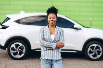 African American woman folded hands with pink ribbon for breast cancer awareness against the car
