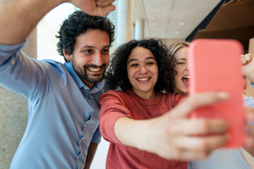 Cheerful woman taking selfie with colleagues on mobile phone