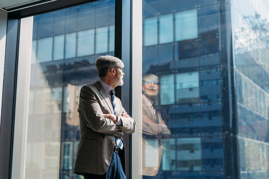 Businessman with arms crossed looking through window in office