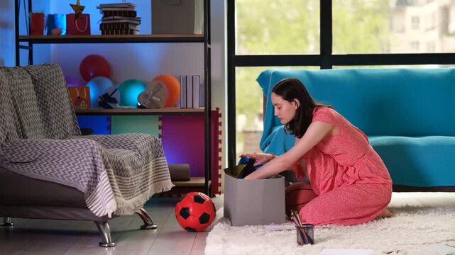 Brunette woman searches frantically through box filled with random items in living room. After finding small lost diary book lady exhales with relief