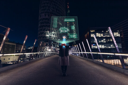Woman wearing VR glasses using tablet PC on bridge in city at night