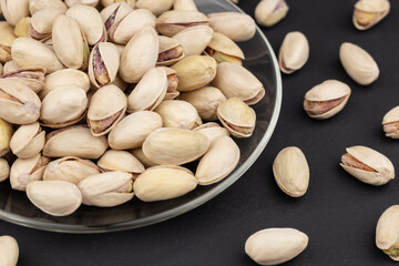 Heap of tasty pistachio nuts on the plate on dark background