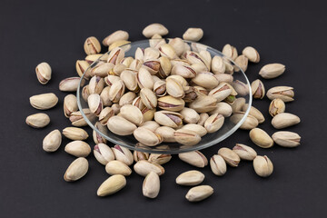 Heap of tasty pistachio nuts on the plate on dark background