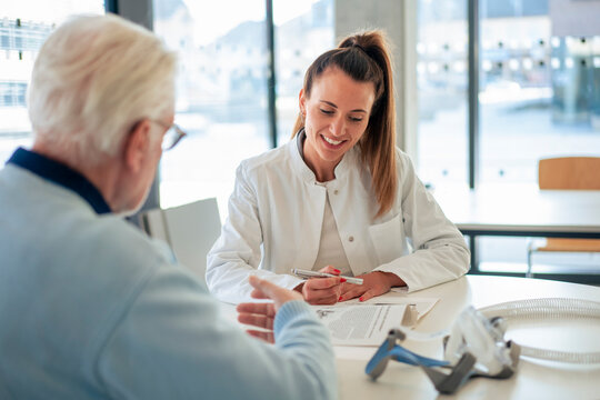 Smiling doctor advising senior patient sitting at desk in clinic