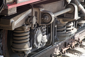 Close-up of a modern freight wagon wheelset with heavy-duty coil springs and brake components on steel rails under natural light. Photo
