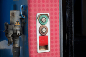Close‑up of red and green electric push buttons on a modern railcar door control panel, highlighting metal housing, connectors and high‑voltage warning symbol in an industrial setting. Photo