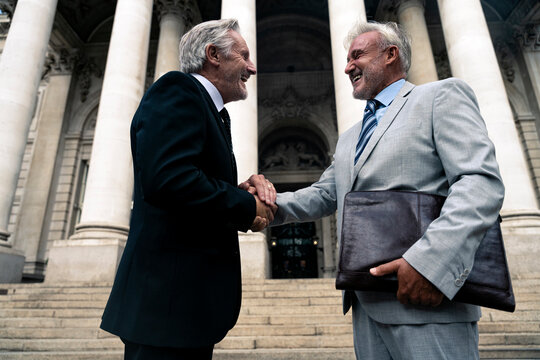 Happy senior businessman holding hands with colleague in front of building