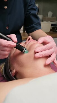 Young woman receiving facial rejuvenation treatment in a beauty salon using modern skincare equipment. Vertical video.