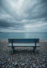 Solitary blue bench overlooking a pebble covered shore under overcast sky with calm sea horizon