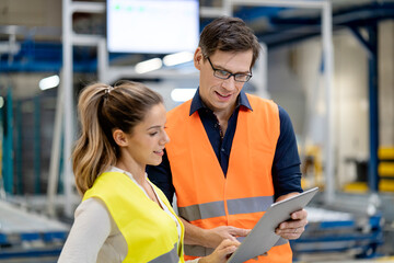 Blue-collar workers in reflective clothing discussing over tablet PC in factory
