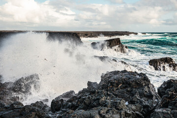 Powerful waves crashing against rugged black volcanic rocks at Brimketill lava rock pool in Iceland