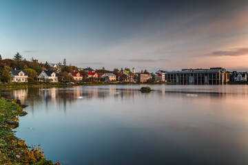 Fototapeta premium A serene sunset over Reykjavík reflecting on the still waters of Tjörnin lake, with traditional Icelandic houses and Reykjavík City Hall against the gradient sky