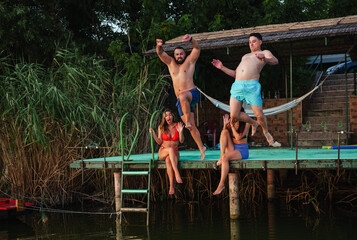 Two men leaping from the dock into the water create a splash, while two women sitting nearby react...