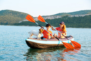 Family canoeing moment on Tsonevo Lake in Bulgaria with scenic background of forested cliffs, peaceful water surface and happy pet-friendly outdoor journey sunset summer.