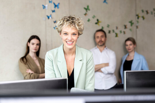 Smiling businesswoman with colleagues in background at workplace