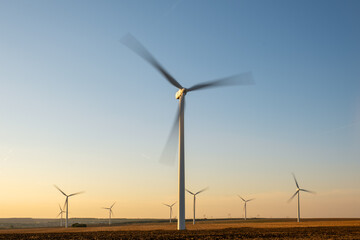 Renewable wind farm in rural region, turbines spinning under clear sky, producing clean energy without emissions, supporting environmental sustainability goals, future of energy captured in scenic