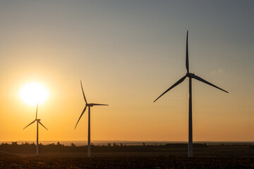 Wind power station across farmland during calm evening, spinning turbine blades generating clean electricity, renewable infrastructure, natural resource usage, sustainable environmental electricity