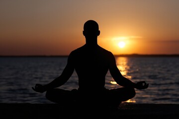 Silhouette of man meditating at sea, Sunset reflection in calm water, Peace and mental clarity in tranquil setting