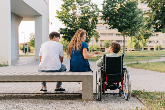 A boy in a wheelchair with his family in the park, back view