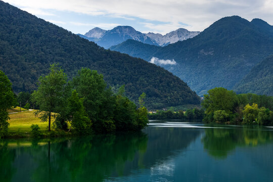 alpine landscape with mountain lake surrounded by lush green forested hills on mountain range backdrop 