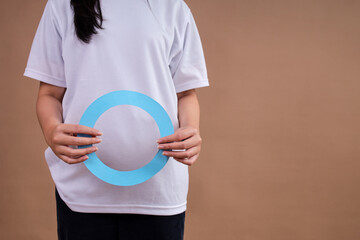 Woman In White Shirt Holding Large Blue Diabetes Awareness Circle Against Brown Background