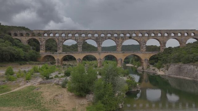 Pont du gard reflecting on gardon river under cloudy sky