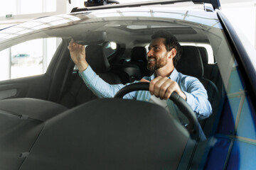 Customer adjusting rearview mirror while sitting in new car at dealership showroom