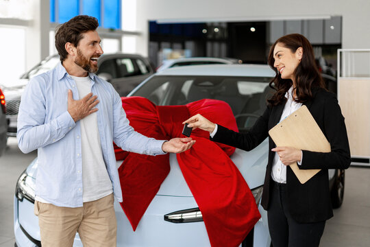 Saleswoman giving car keys to excited man in dealership