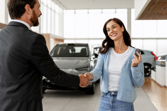 Woman buying new car shaking hands with car dealer - Powered by Adobe